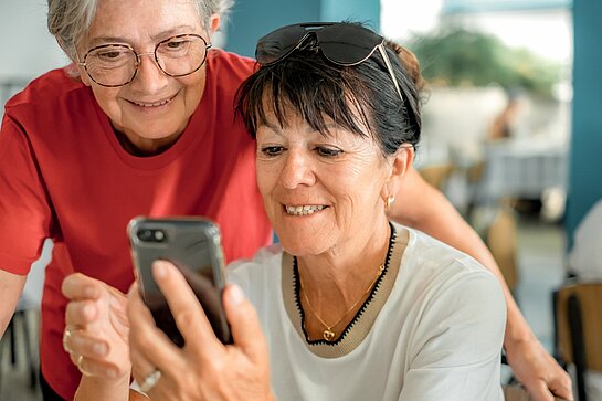 Attractive couple of elderly caucasian women sitting at restaurant table looking on mobile phone the online menu to select food and drink